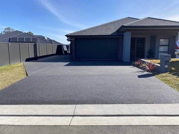 Modern home with freshly paved concrete driveway installed by concrete contractors in Olathe KS, featuring dark gray surface and solar panels on roof