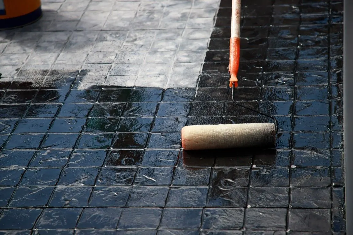 Concrete sealing in progress with a paint roller on tiled outdoor surface by concrete contractors in Olathe KS